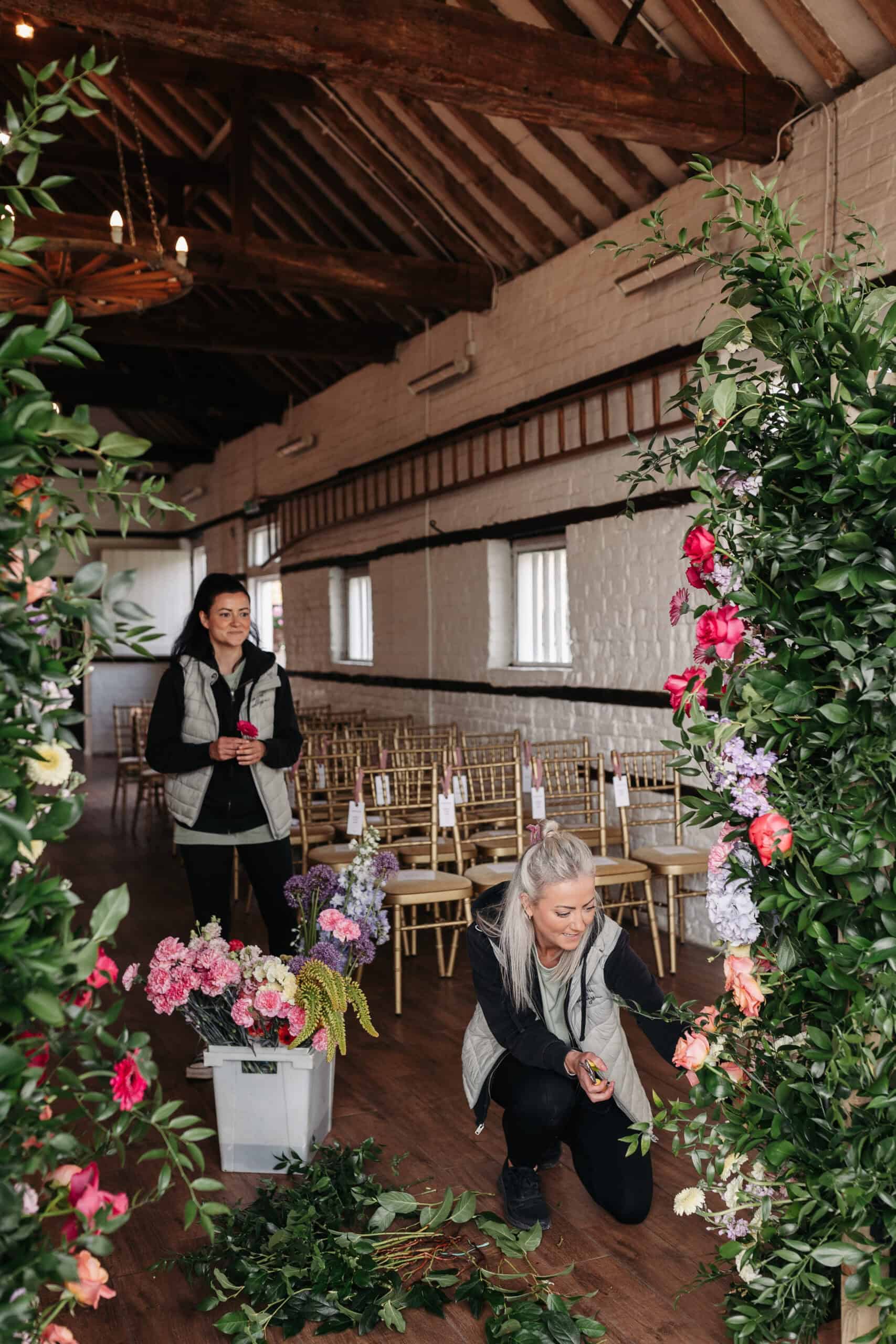 Two florists from Ever After Weddings setting up the small barn at Lillibrooke Manor, arranging vibrant flowers and greenery to create a stunning ceremony backdrop.